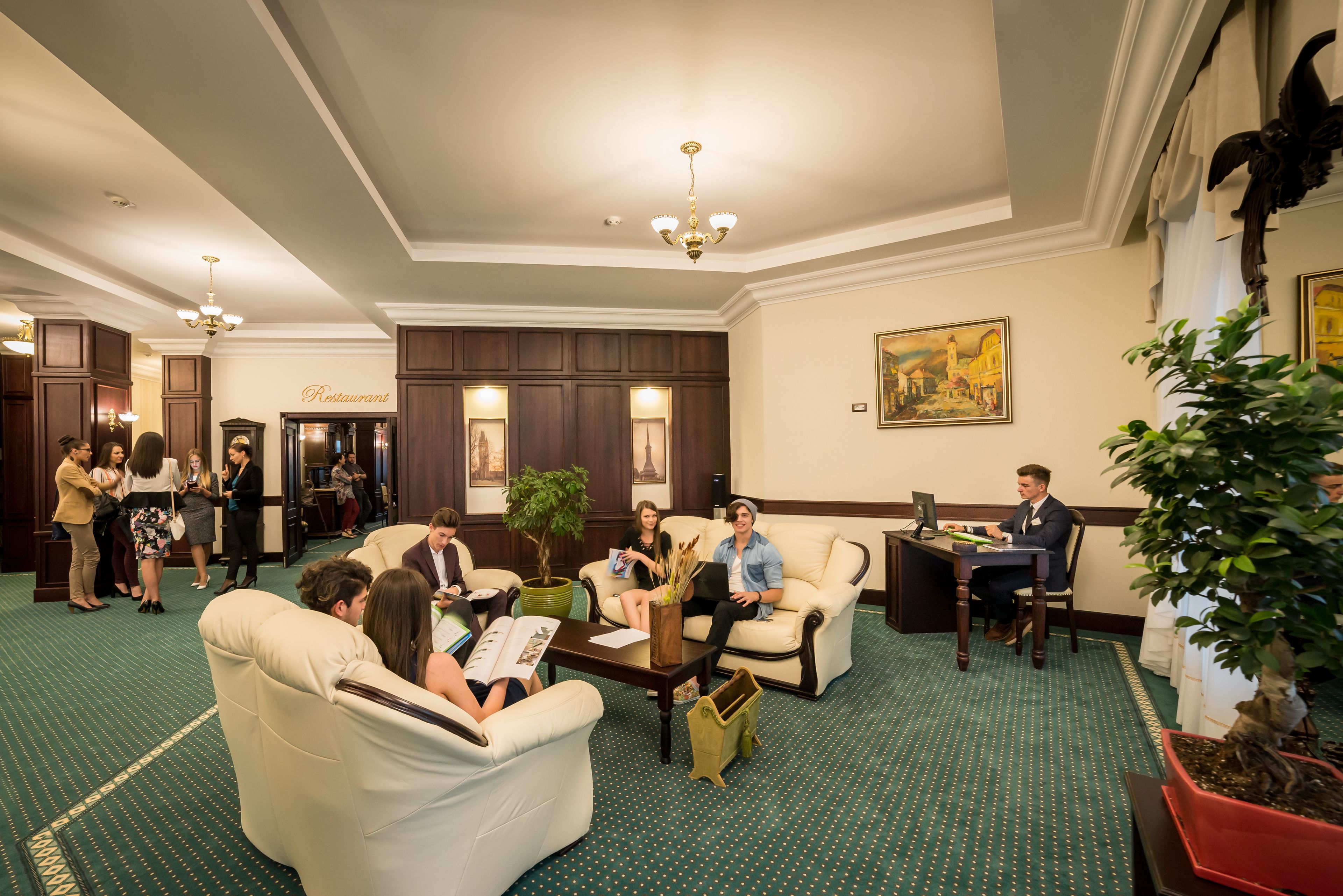 A hotel lobby with a green carpet, leather sofas, a coffee table, and a dining area.