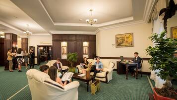 A hotel lobby with a green carpet, leather sofas, a coffee table, and a dining area.