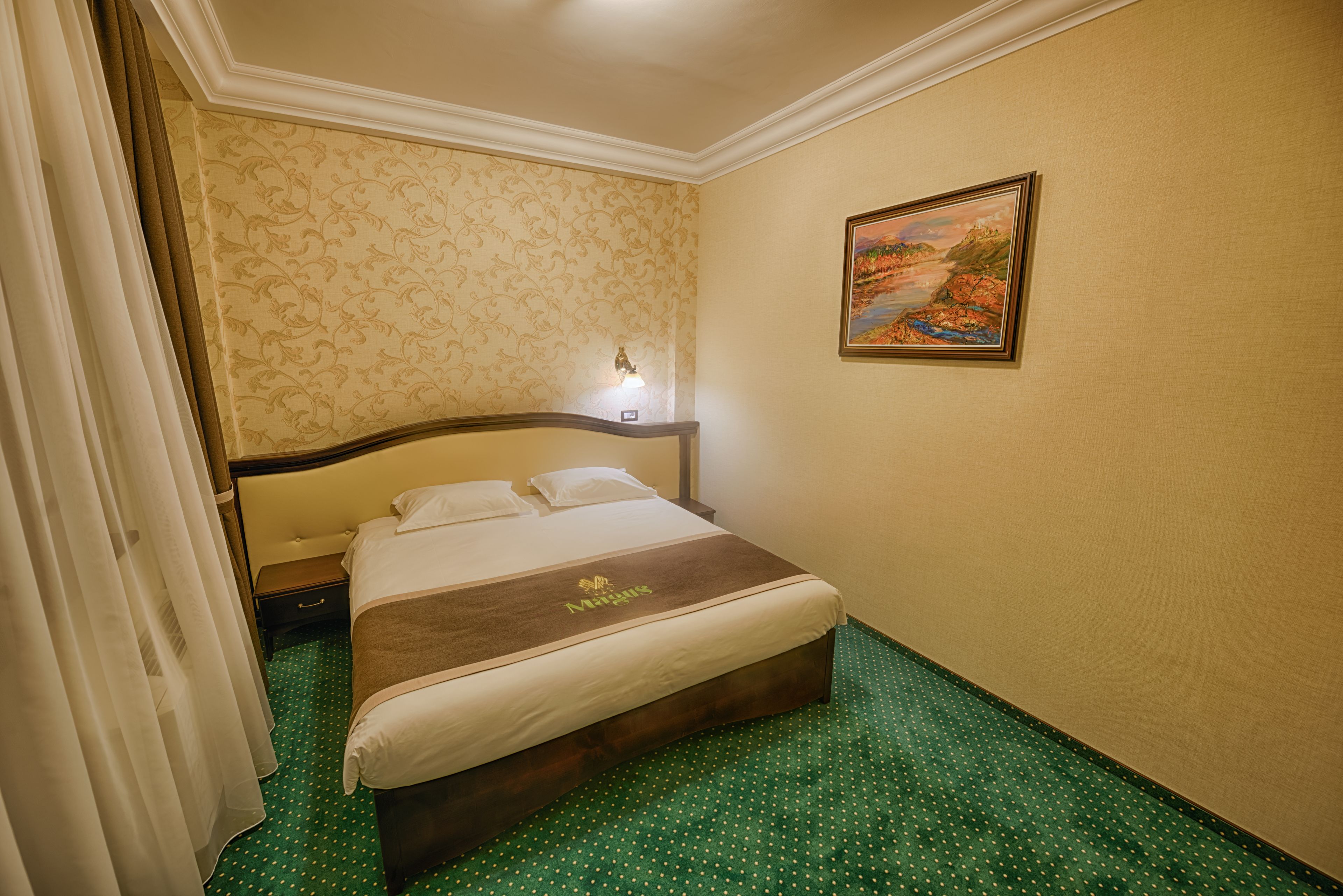 Ein Hotelzimmer mit einem Bett, einem Nachttisch, einer Lampe, einem Bild an der Wand und einem grünen Teppich mit Punkten.