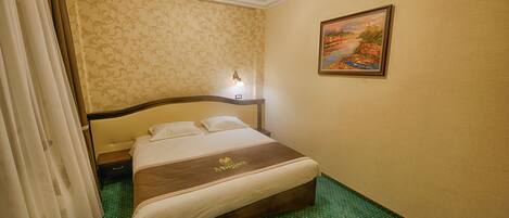 A hotel room with a bed, a nightstand, a lamp, a painting on the wall, and a green polka dot carpet.