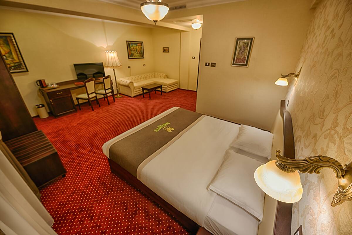 A hotel room with a large bed, a desk with a chair, a sofa, and a television.