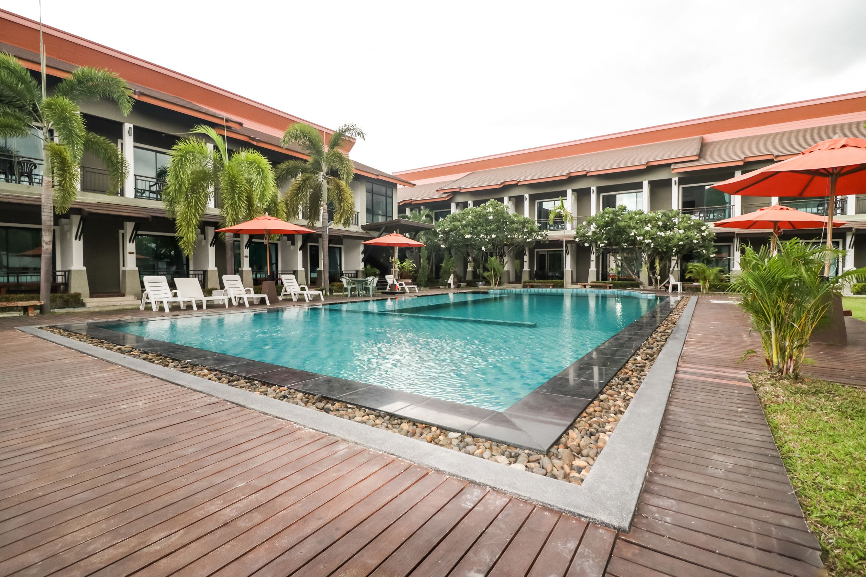Un espace piscine d’hôtel avec des chaises longues et des parasols, entouré d’une terrasse en bois et de verdure.