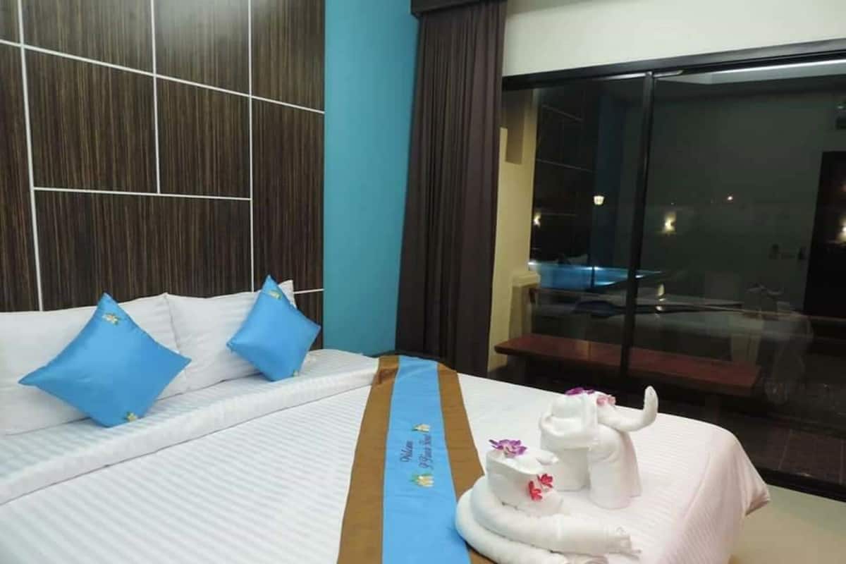 Quarto de hotel com cama, duas almofadas azuis, colcha branca, faixa decorativa azul e escultura de toalha branca, com vista para uma piscina através de uma porta de vidro.