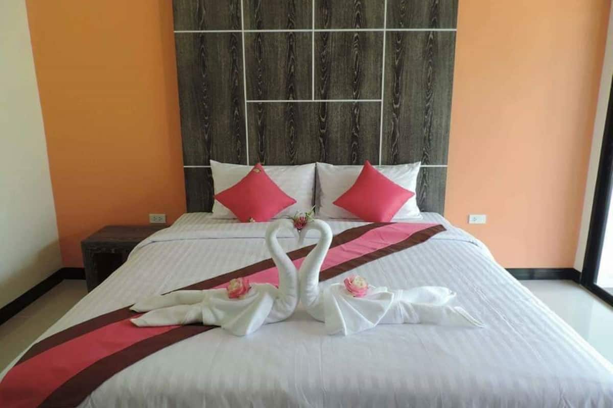 Quarto de hotel com uma cama grande, duas almofadas vermelhas, cabeceira de madeira e um arranjo decorativo de cisnes na cama.