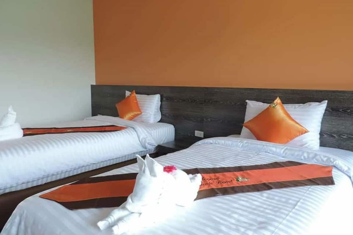 Quarto de hotel com duas camas, cada uma com roupa de cama branca e almofadas laranja.