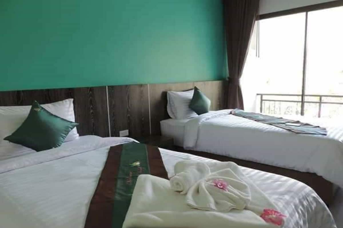 Quarto de hotel com duas camas, uma parede verde e uma janela com cortinas.