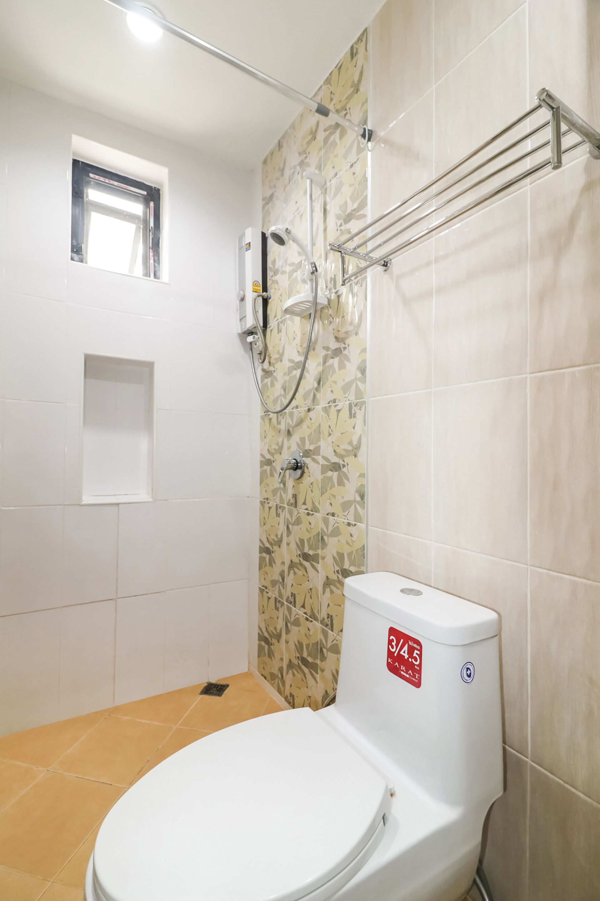 Et badeværelse med toilet, bruser og et lille vindue.