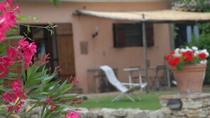 A house with a stone wall, a patio with a table and chairs, and a garden with pink flowers. - Agriturismo Podere Conte Ràcani (Amelia)