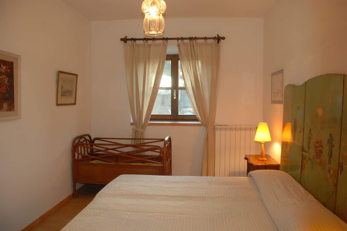 A bedroom with a wooden bed, a window with curtains, a radiator, and a lamp on a bedside table.