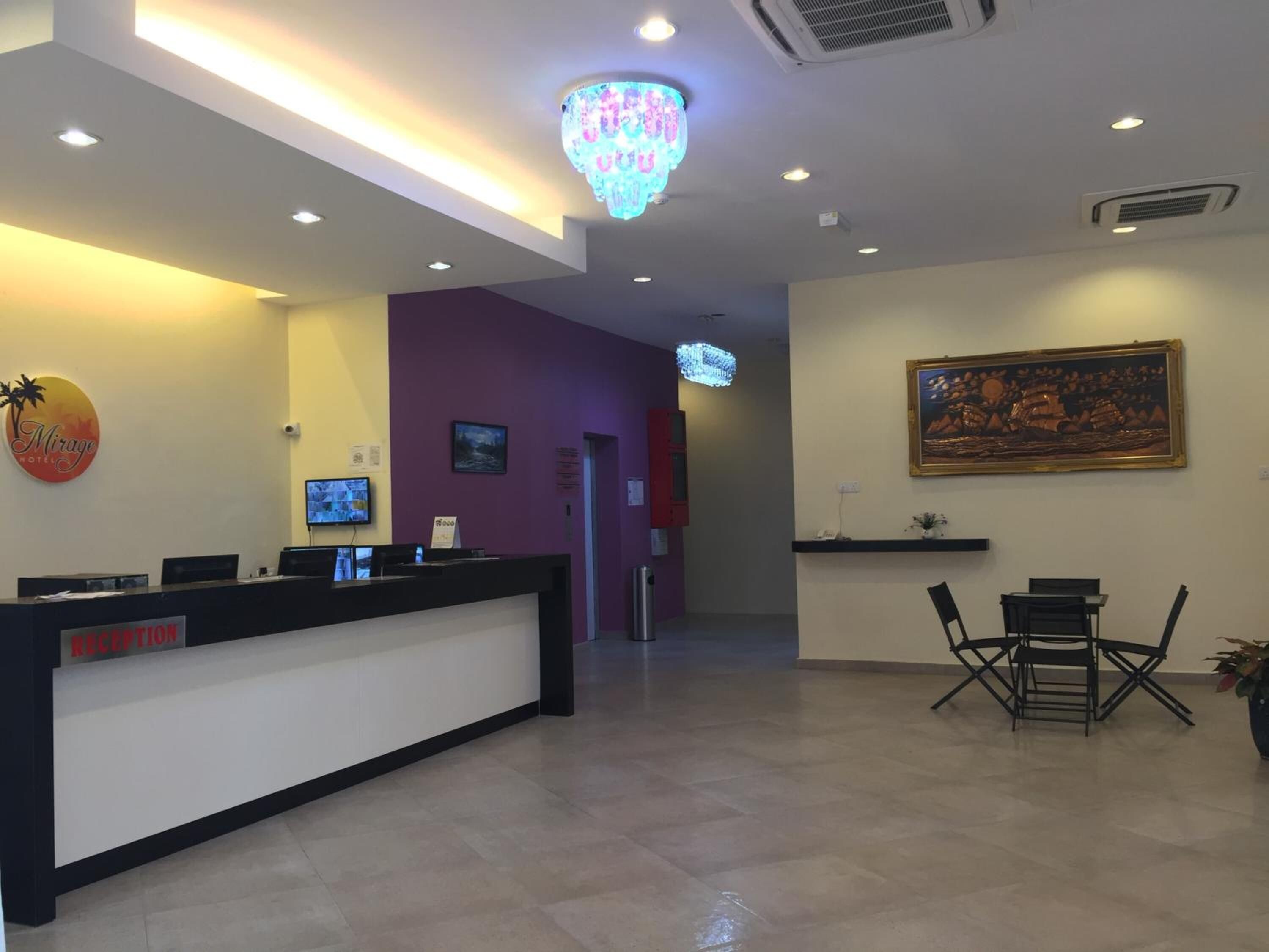 A hotel reception area with a reception desk, a television, a painting on the wall, and a chandelier.