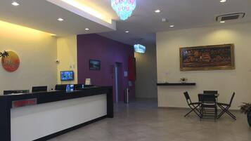 A hotel reception area with a reception desk, a television, a painting on the wall, and a chandelier.