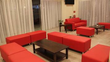 Un hall de hotel con sofás rojos, una mesa de centro de madera y un televisor montado en la pared.