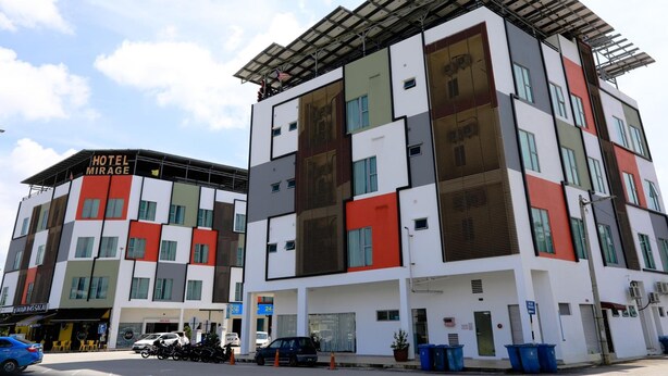 A multi-story hotel with a modern design, featuring a mix of white, gray, and red panels, and a flat roof with solar panels.
