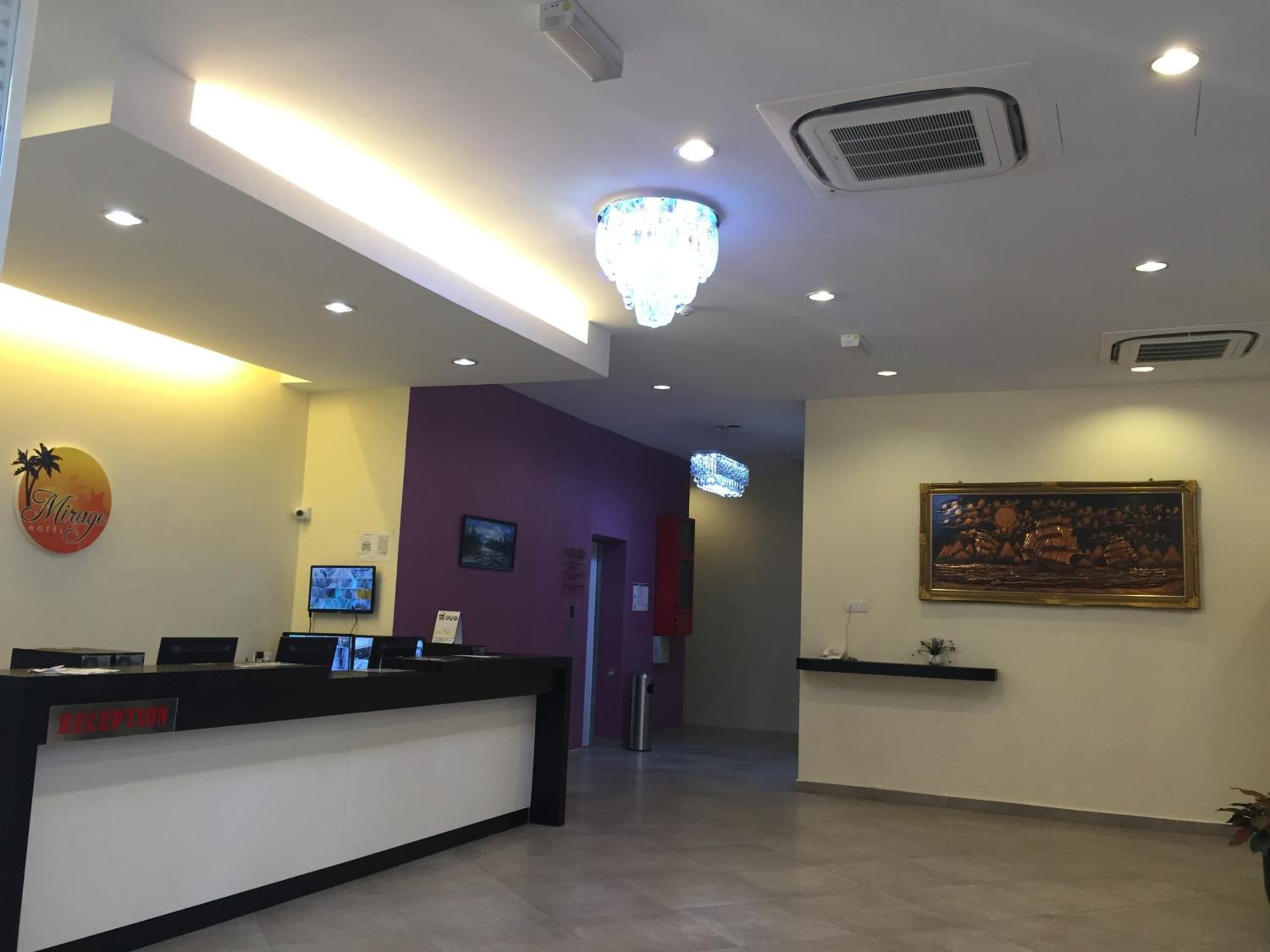 Een hotel receptie met een receptiebalie, een kroonluchter, een ingelijst kunstwerk en een bordje met de tekst receptie.