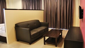 A modern hotel room with a dark brown sofa, a wooden coffee table, and a TV mounted on the wall.