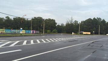 Una intersección de calles con varios carriles y semáforos. Hay vallas publicitarias y señales a un lado de la vía.