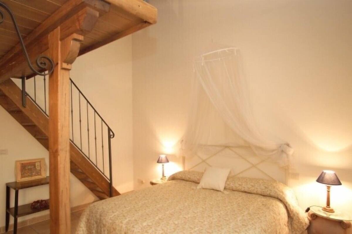 A bedroom with a wooden staircase, a bed with a canopy, and two bedside lamps.