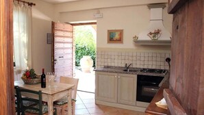 Una cocina con comedor, que incluye una mesa de madera, sillas, una botella de vino y una cesta de fruta.