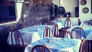 A restaurant with multiple tables set for dining, wooden chairs, and a stone wall. - Antica Pensione Pinna (Castelsardo)