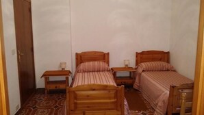 A small, compact room with two wooden beds, each with a nightstand and a lamp. The room has a patterned floor and a wooden door. - Antica Pensione Pinna (Castelsardo)
