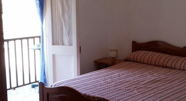 Une chambre à coucher avec un lit, une table de chevet, une lampe, une fenêtre avec des rideaux et une porte.