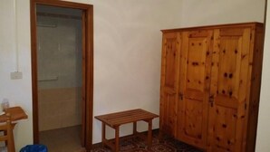 A room with a wooden wardrobe, a small wooden table, and a door leading to another room. - Antica Pensione Pinna (Castelsardo)