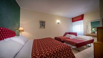 Habitación de hotel con dos camas, una mesita de noche, una lámpara, un cuadro en la pared y una ventana con cortinas.
