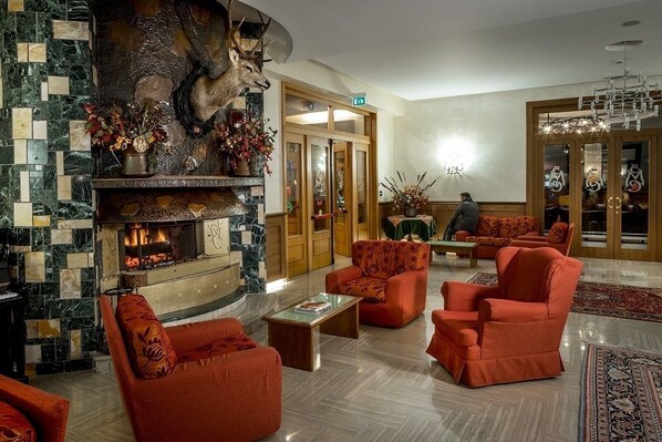 Un vestíbulo con chimenea de piedra, asientos tapizados en rojo y un candelabro.