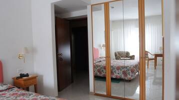 Una camera d'albergo con un'armadio in legno, un letto con lenzuola a motivi floreali, un comodino con una lampada e una sedia nell'angolo.