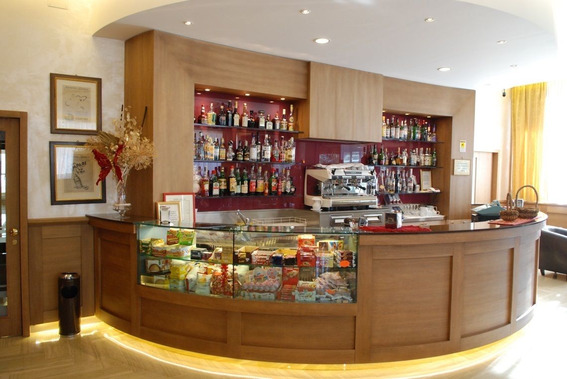 Zona de recepción de hotel con un mostrador curvo, una vitrina con aperitivos y estantes con bebidas embotelladas.