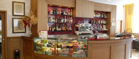 Zona de recepción de hotel con un mostrador curvo, una vitrina con aperitivos y estantes con bebidas embotelladas.