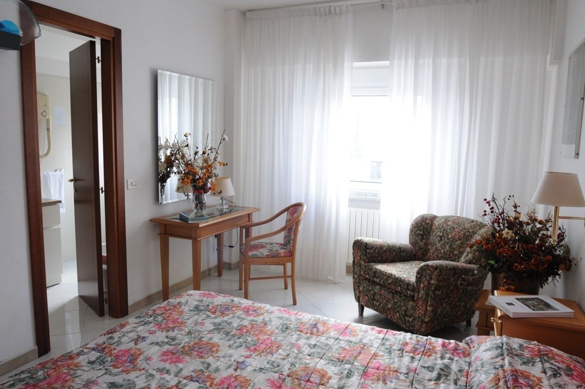 A hotel room with a bed, a desk, a chair, and a window with curtains.