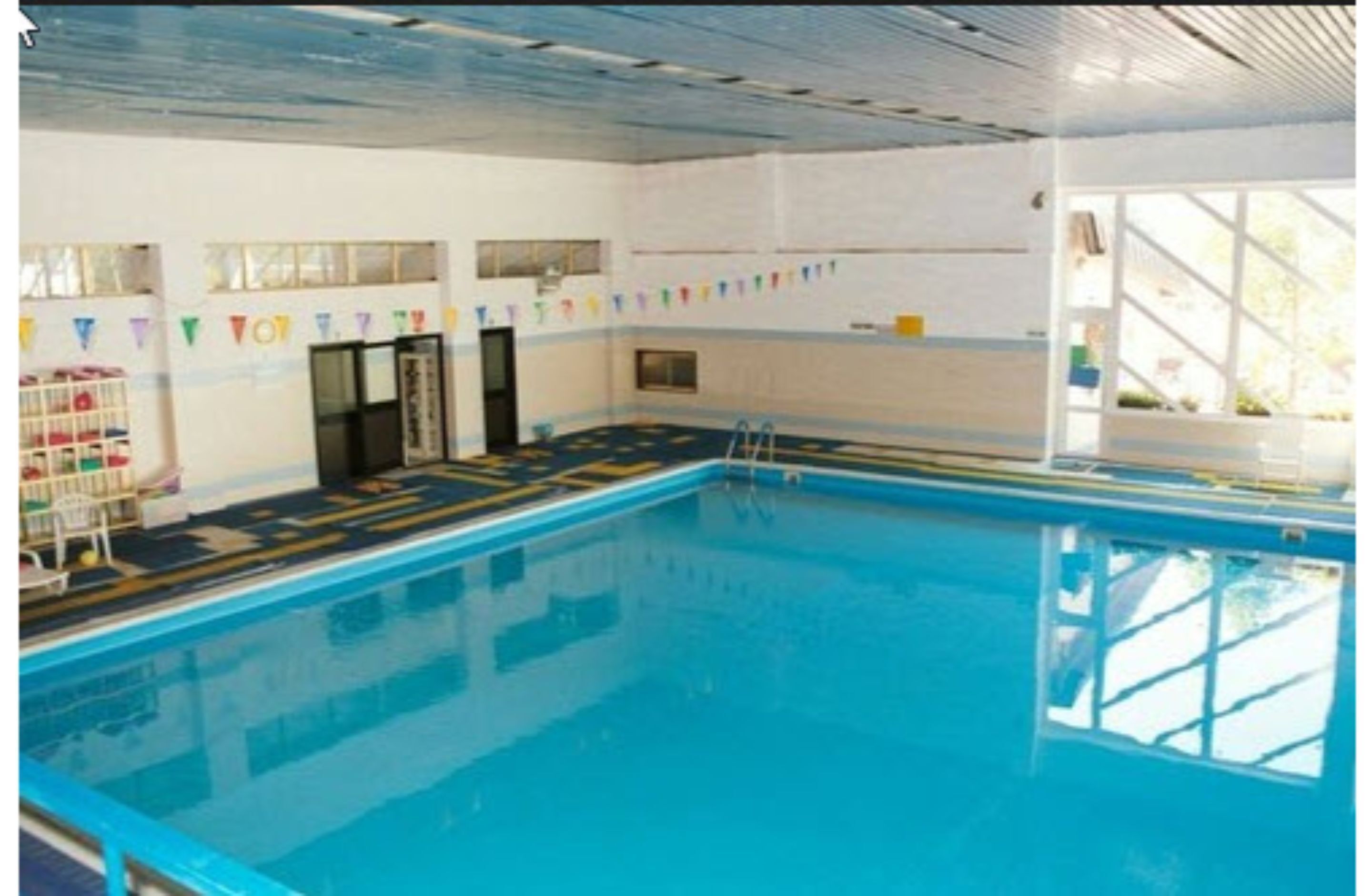 An indoor swimming pool with clear lanes, a ladder, and a tiled floor.