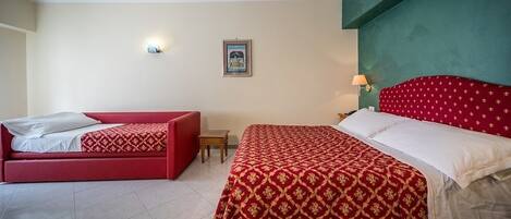 Una habitación de hotel con cama y sofá rojos, una mesita pequeña y una lámpara fijada a la pared.