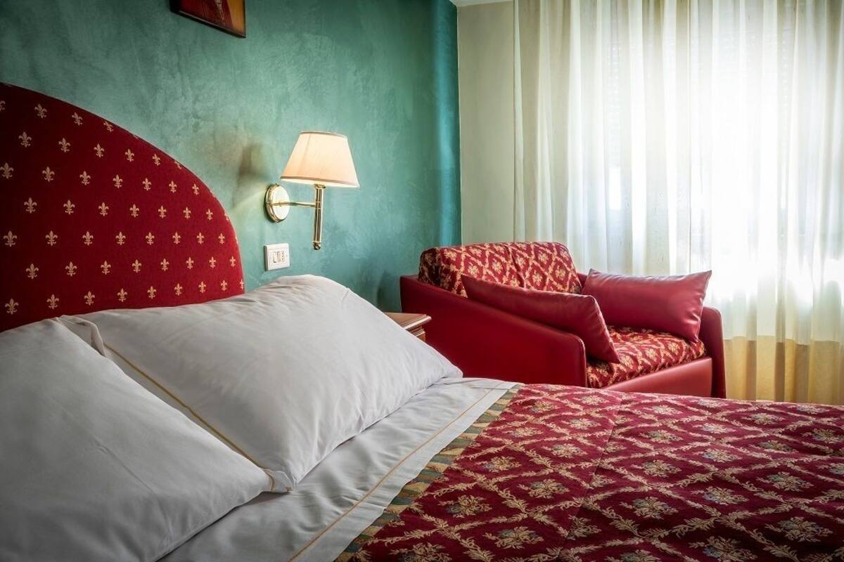 Une chambre d’hôtel avec un lit, un fauteuil rouge et une table de chevet avec une lampe.