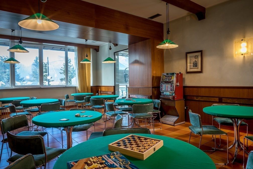 A cozy indoor setting with multiple green tables and chairs, a chessboard, and a vintage jukebox.