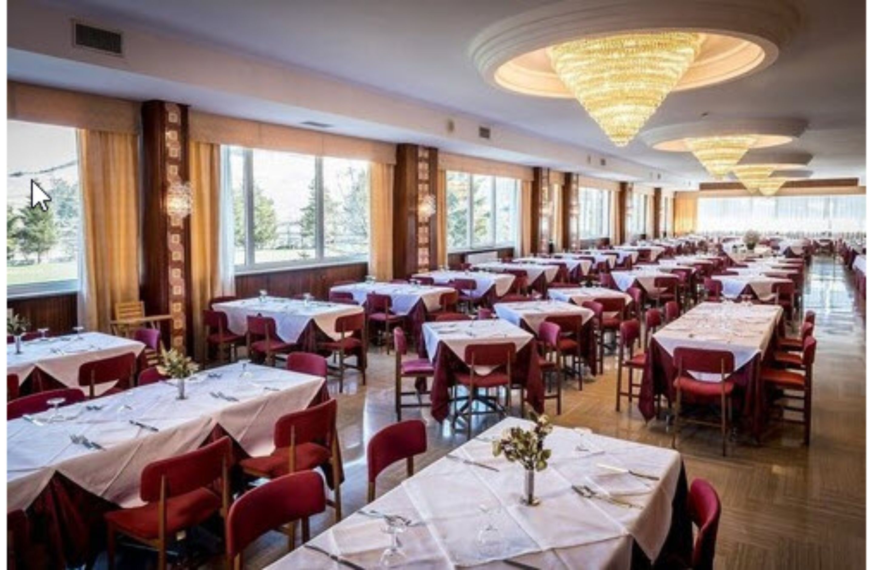 Una sala da banchetto con numerosi tavoli imbanditi, ampie finestre e un lampadario centrale.