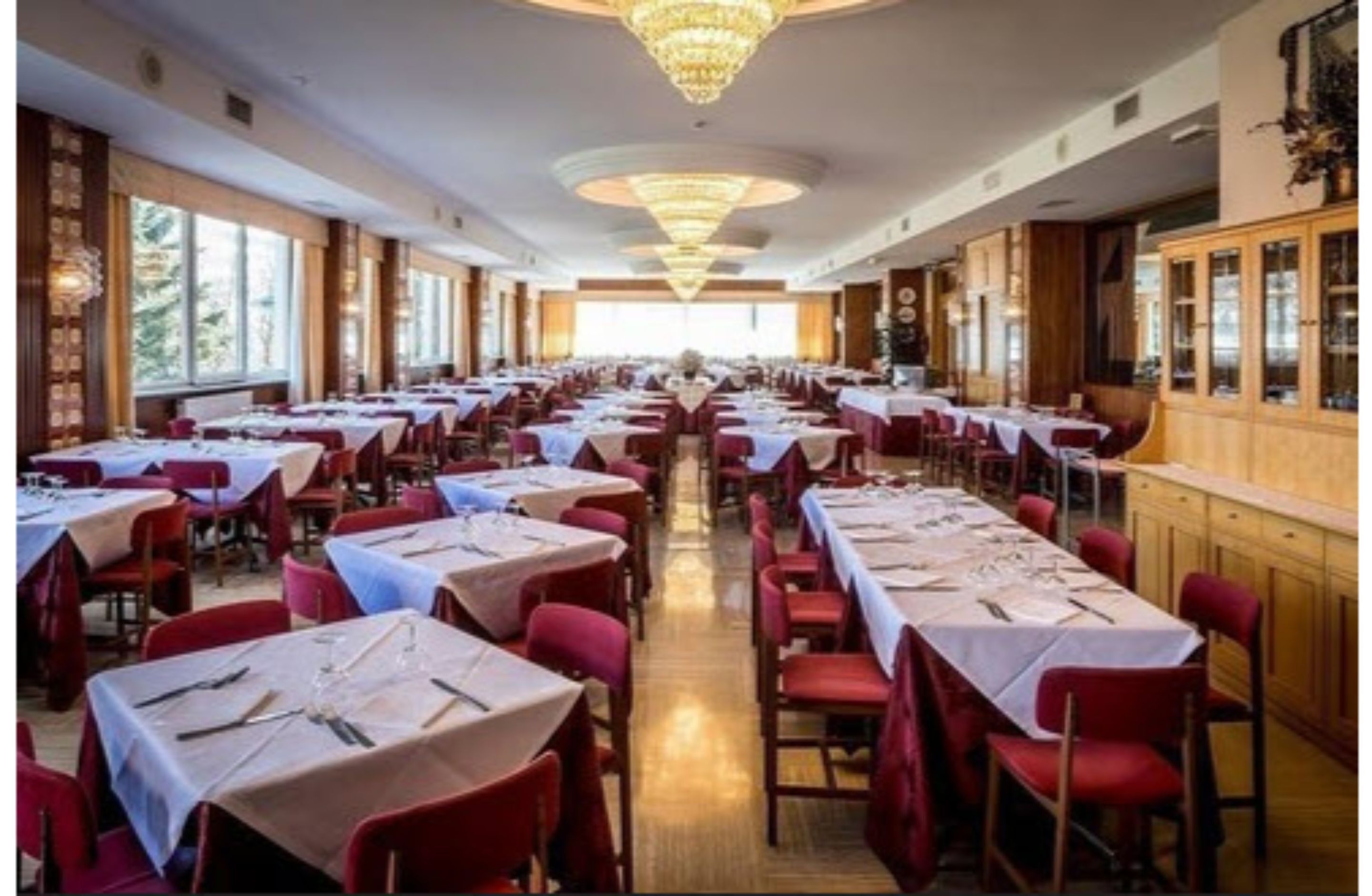 A large banquet hall with long tables set for dining, wooden paneling, and large windows.
