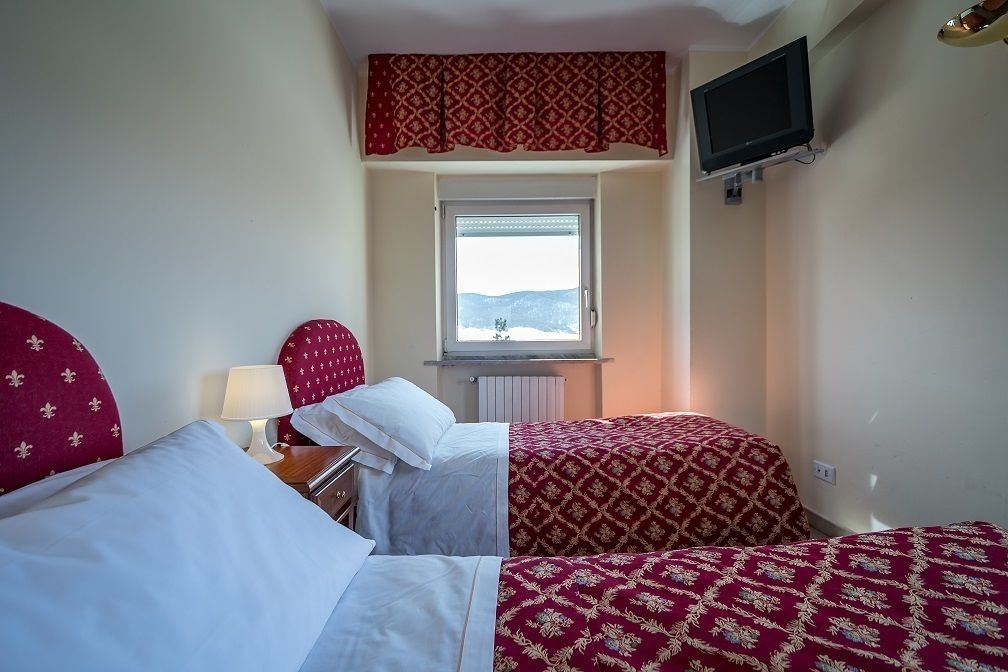 A hotel room with two beds, a TV mounted on the wall, and a window with a view of the mountains.