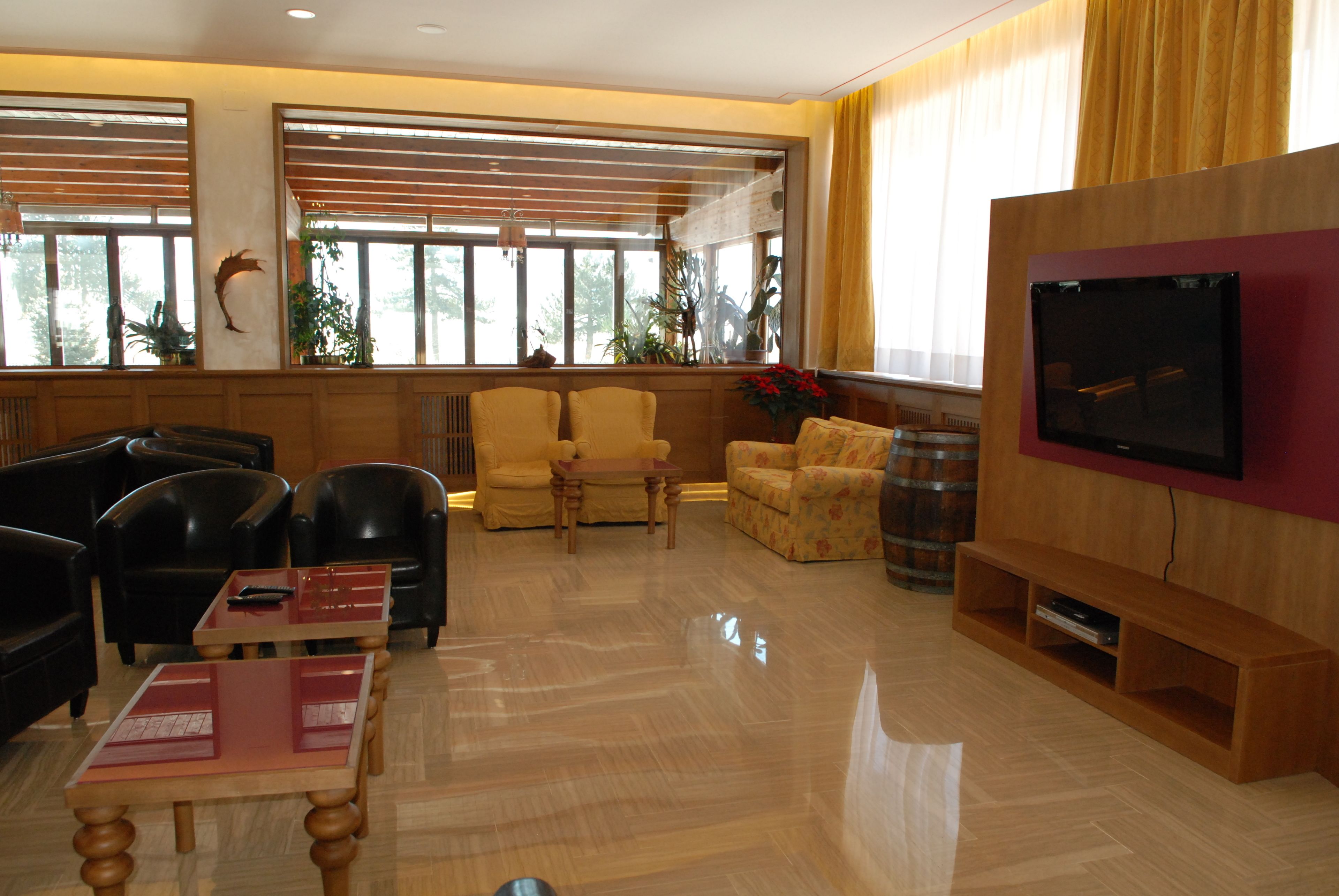 A spacious lobby with a polished wooden floor, comfortable seating, a flat-screen TV, and large windows with blinds.