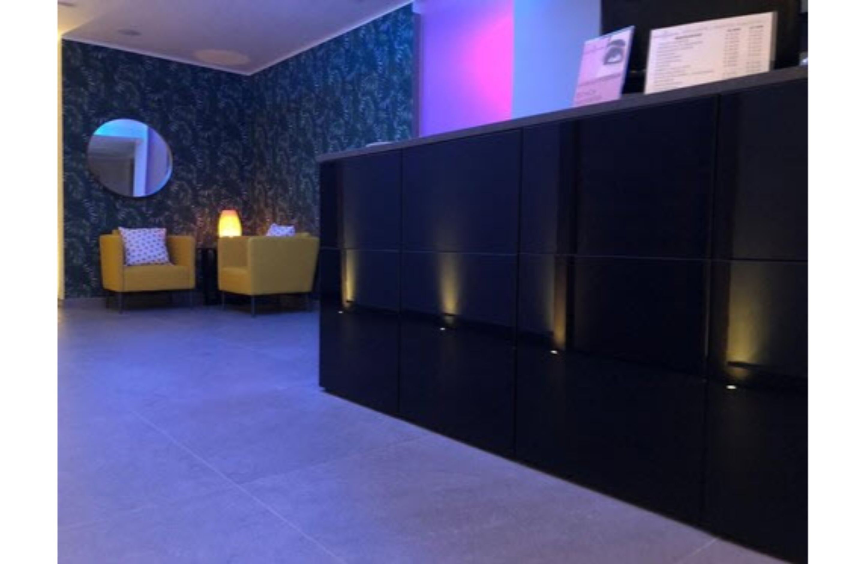 A reception area with a dark blue patterned wall, a round mirror, and two yellow armchairs.