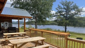 A wooden deck with picnic tables overlooking a lake. - Air-Dale Fishing and Hunting (Unorganized North Algoma)