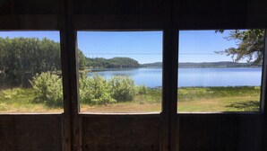A room with three large windows offering a view of a lake and forest. - Air-Dale Fishing and Hunting (Unorganized North Algoma)