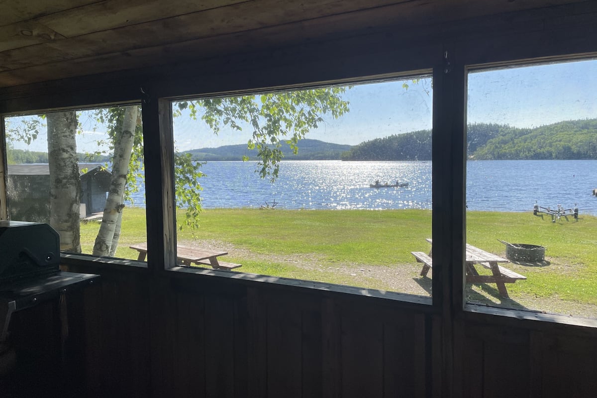 A cabin with a view of a lake, a picnic table, and a grill.