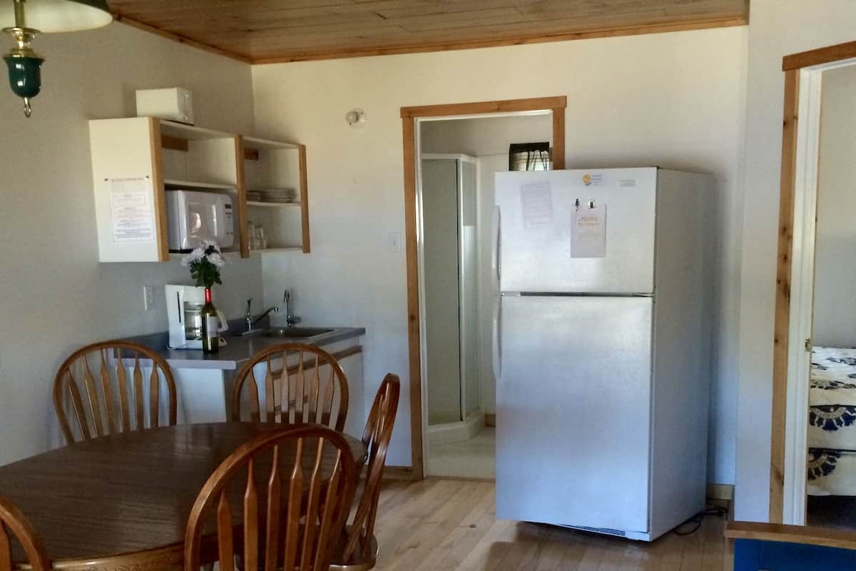 A compact kitchen with a refrigerator, microwave, and wooden cabinets. There is a dining table with chairs and a small kitchenette area.