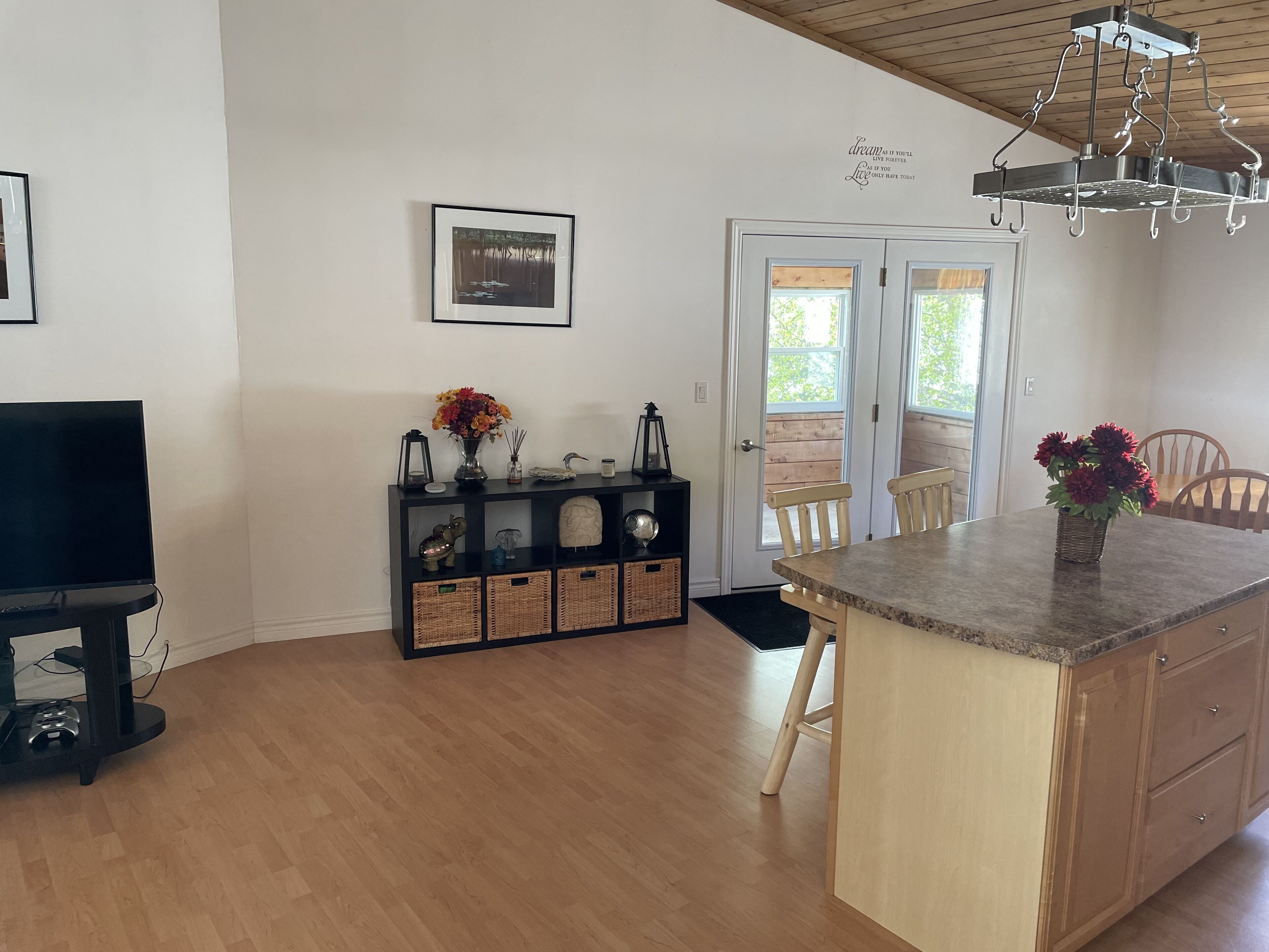 A kitchen with a wooden island, a black entertainment unit, and a dining area with wooden chairs.