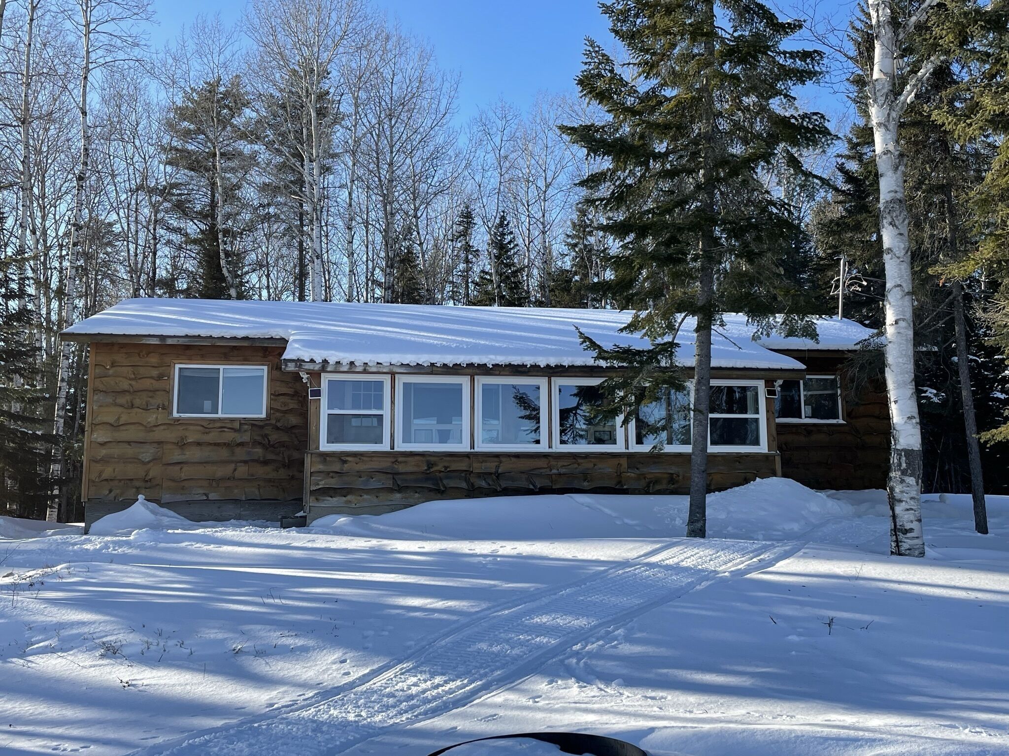 Une cabane en rondins surmontée d’un toit en métal, entourée de neige et d’arbres.