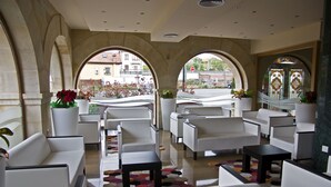 A modern lounge area with white sofas and armchairs, large windows with arches, and potted plants. - Hotel Felisa Spa (Santillana del Mar)