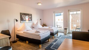 A hotel room with two beds, a desk, a chair, a floor lamp, and a view of the outside balcony.