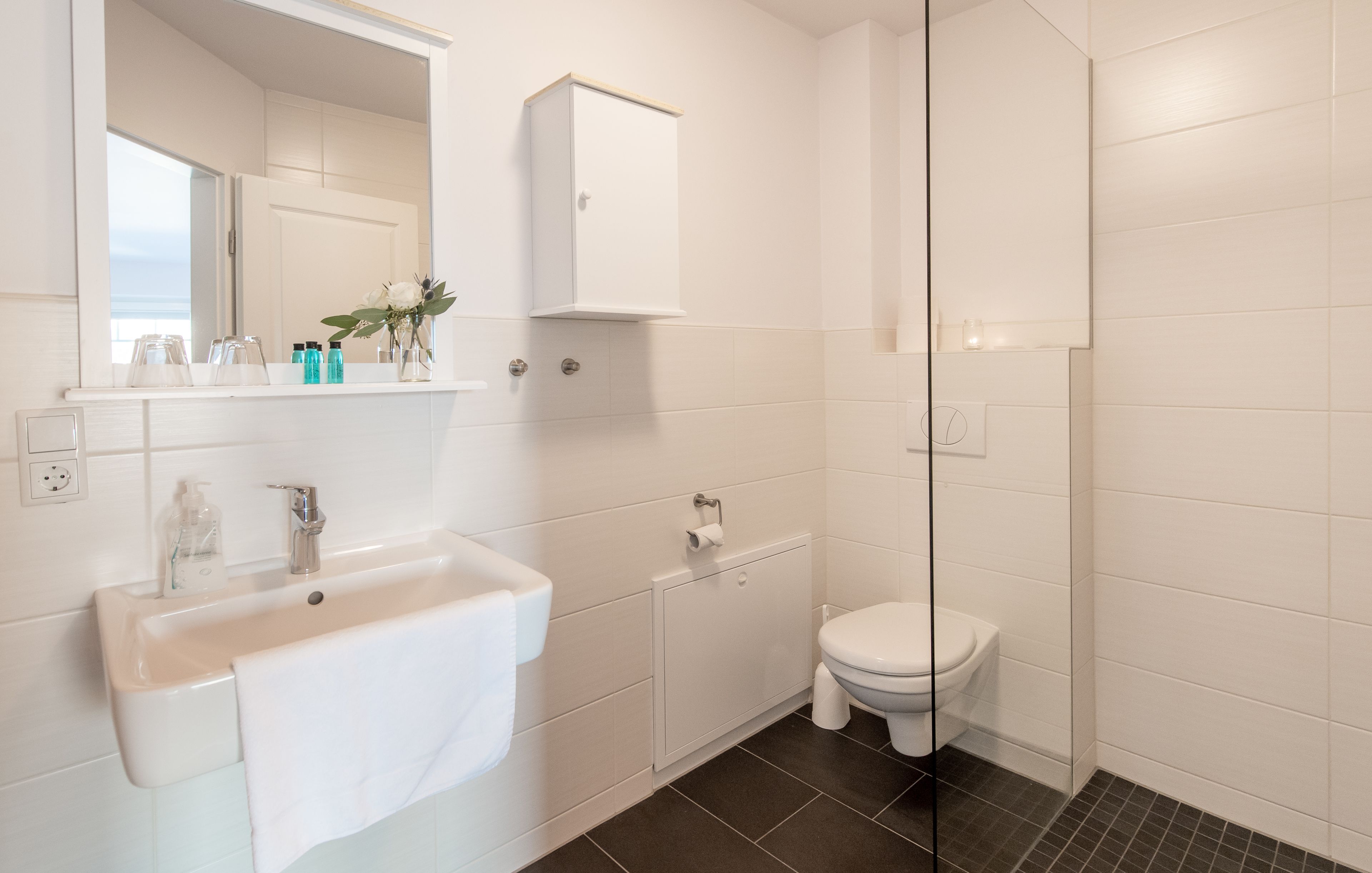 Une salle de bain moderne avec un lavabo, des toilettes et une douche, le tout de couleur blanche.
